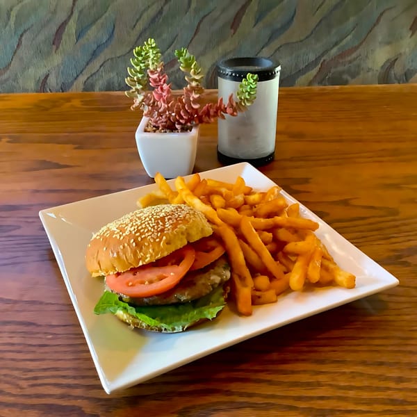 A hamburger with lettuce and tomato, served with a side of golden fries on a white plate.