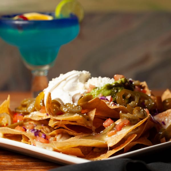 El Jardin's nachos with jalapeños, sour cream, guacamole, and a blue margarita in the background.